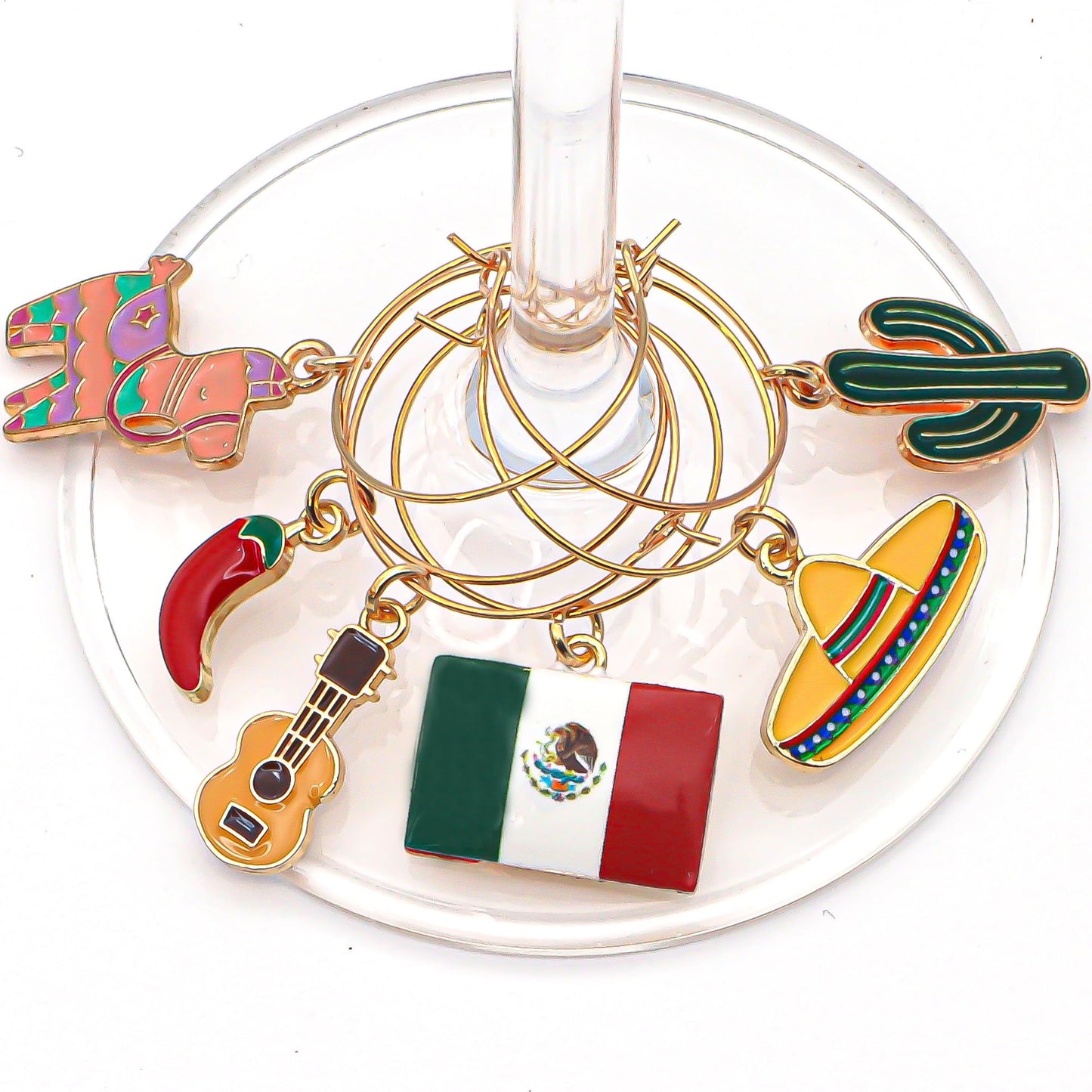 A set of Mexico Wine Charms featuring Piñata, Mexican Flag, Chili Pepper, Cactus, Guitar, and Sombrero hooked on the wine glass.