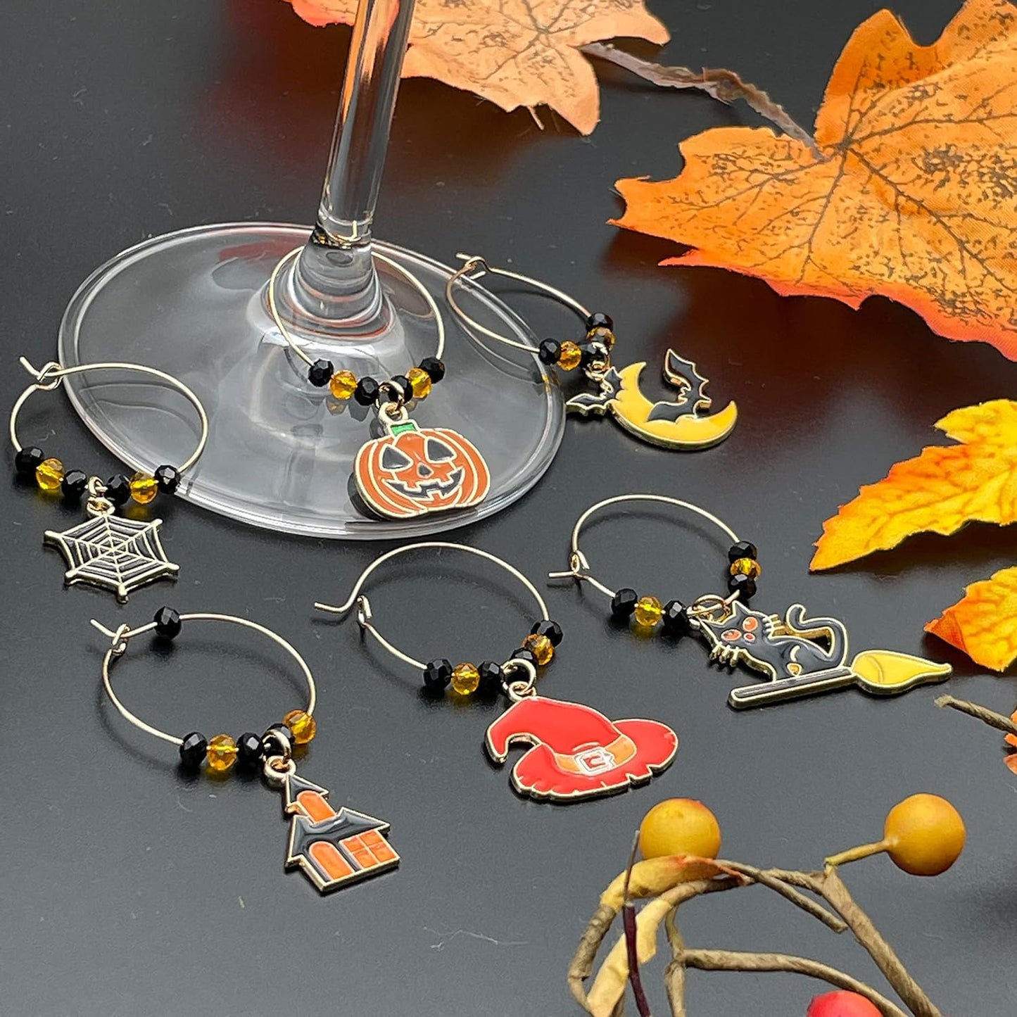 Halloween Wine Charms set of witch hat, bat, spider web, jack-o'-lanterns, and black cat on a black surface