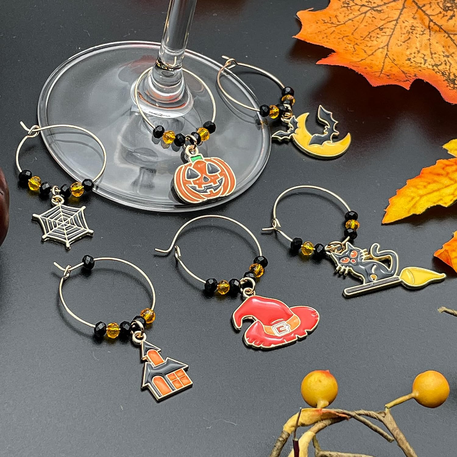 Halloween Wine Charms set of witch hat, bat, spider web, jack-o'-lanterns, and black cat on a black surface