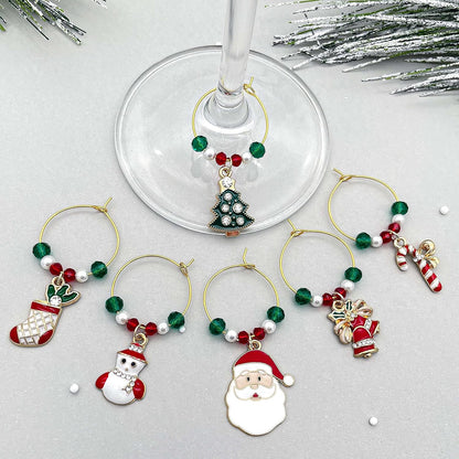 A set of Christmas Wine Charms featuring including Santa, Candy Cane, Snowman, Christmas Bells, Stocking, and Christmas Tree on a grey surface.