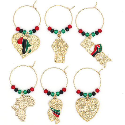 Africa Wine Charms on a white surface representing  Pan-African Flag, a map of the African continent, a Heart with "BLM" engraved, a Girl wearing an African headwrap, a Clenched Fist, and the Black Power Symbol.